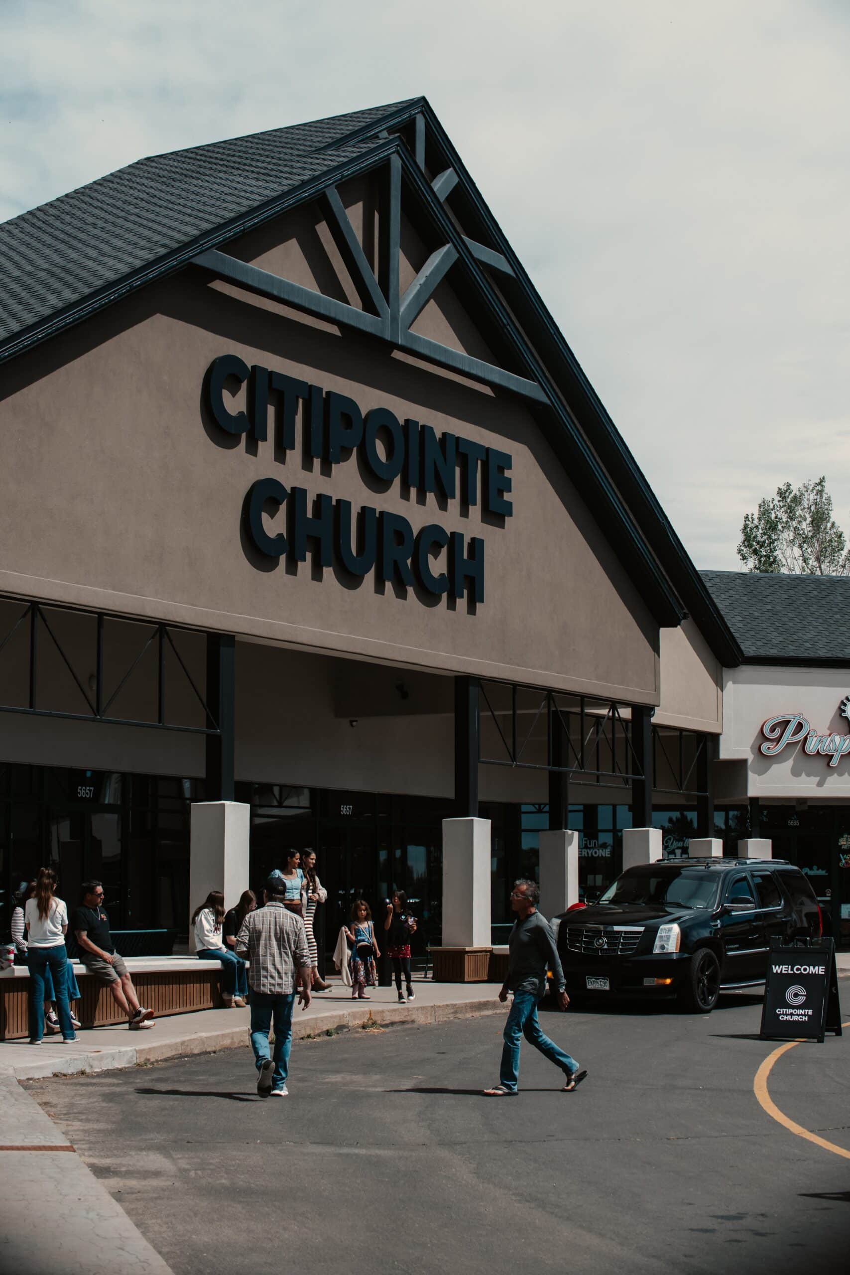 The facade of Citipointe Church is visible, showcasing large signage with the name prominently displayed. People are gathered outside in casual attire, and a black truck is parked nearby on a paved area.